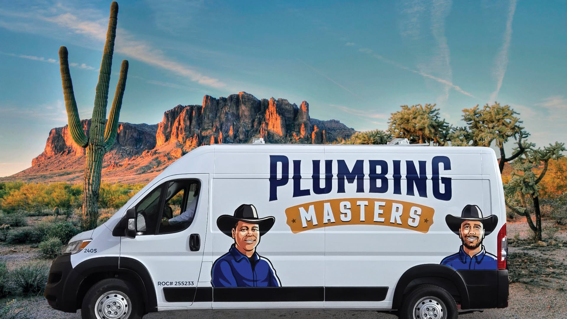 White Plumbing Masters service van with bold blue logo and cartoon plumbers, set against a desert landscape with cacti and red rock mountains.
